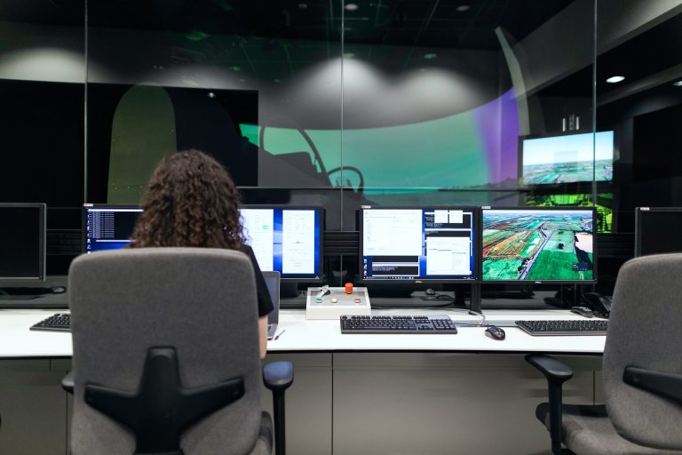 A woman seated at a desk, working with three computers arranged in front of her.