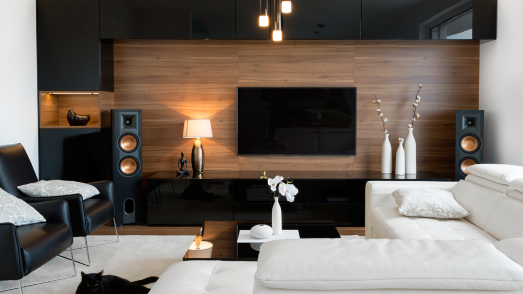 A modern living room decorated with black and white accents and large speakers near the TV.