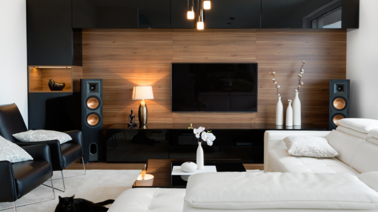 A modern living room decorated with black and white accents and large speakers near the TV.