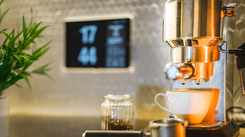 A fancy coffee maker with a smart home panel behind it.