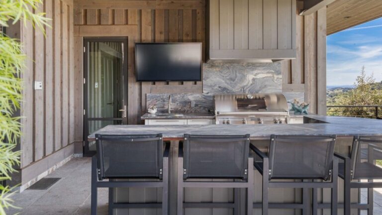 An outdoor kitchen in a modern luxury home with a TV.