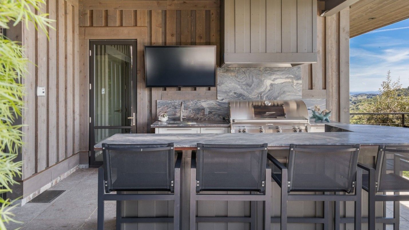 An outdoor kitchen in a modern luxury home with a TV.