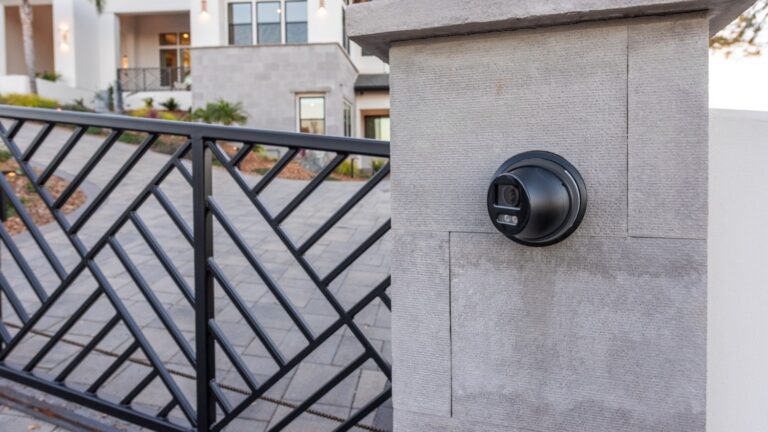 The gate to a luxurious home with a surveillance camera installed out front.