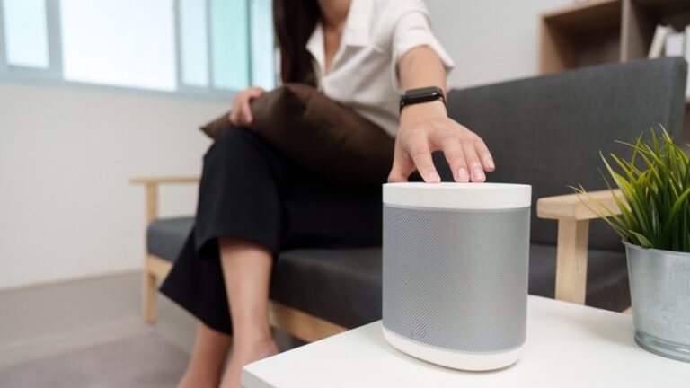 A woman sitting on a couch touches the top of a home audio speaker.
