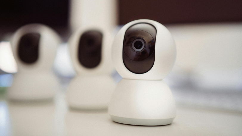 A modern surveillance camera with a white, circular housing and a large black lens.