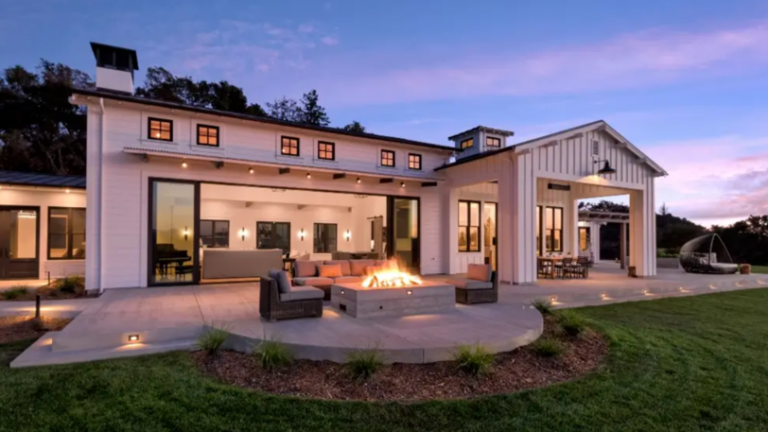 A large, modern home with a roaring outdoor fire pit surrounded by comfortable seating.