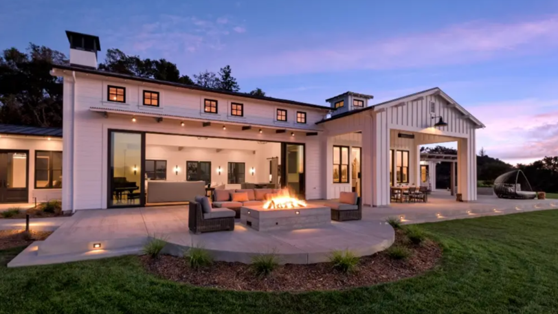 A large, modern home with a roaring outdoor fire pit surrounded by comfortable seating.